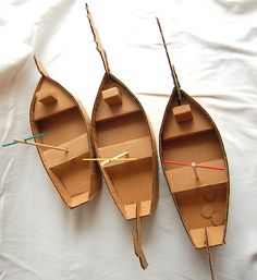 three cardboard boats sitting on top of a white sheet covered ground with string attached to them