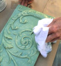 a person is using a cloth to clean a piece of green art decoupholing