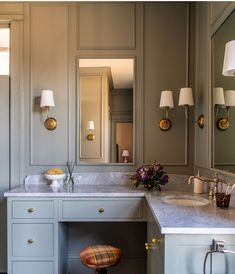 a bathroom with gray walls and white counter tops, gold fixtures and two stools in front of the sink