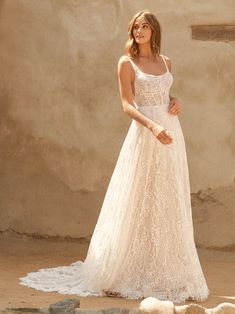 a woman wearing a white dress standing in front of a stone wall and looking at the camera