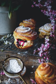 several pastries on a cooling rack with powdered sugar and purple flowers in the background