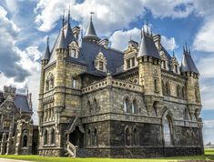 an old castle like building with many windows and spires on the top floor, under a cloudy blue sky