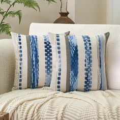 a white couch with blue and gray striped pillows on it's back, next to a potted plant