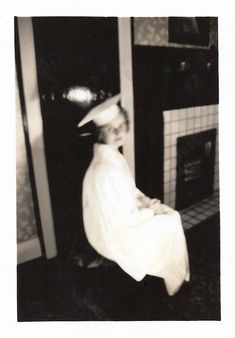 black and white photograph of a woman sitting in front of a fireplace