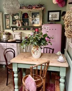 a pink refrigerator in a kitchen next to a table with chairs and flowers on it