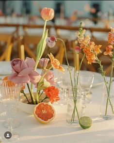 an arrangement of flowers and fruit in vases on a white table cloth at a wedding reception