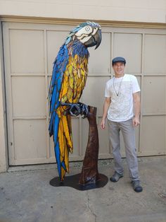 a man standing next to a large colorful parrot on top of a wooden stick in front of a garage door