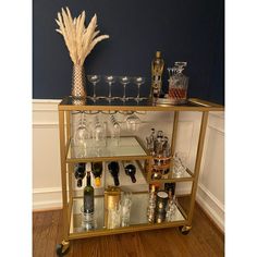 a gold bar cart filled with wine glasses and liquor bottles on top of a hard wood floor