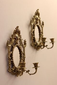 two ornate gold wall sconces hang on the wall next to a candle holder