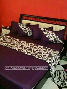 a bed with purple sheets and pillows in a room that is painted orange, black and white