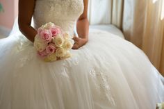 a woman in a white wedding dress holding a bouquet of pink and yellow flowers on her lap