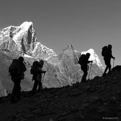 black and white photograph of hikers on the side of a mountain with snow capped mountains in the background