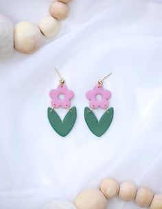 pink and green flower shaped earrings sitting on top of a white table next to shells