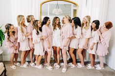 a group of women standing next to each other in front of a mirror wearing pink dresses