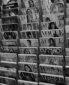 many magazines stacked on top of each other in front of a store window with people's faces