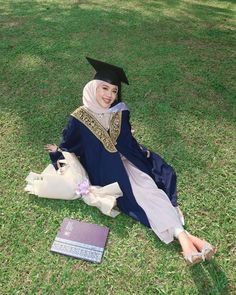 a woman sitting on the ground wearing a graduation gown and holding a book in her hand