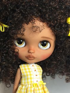 a close up of a doll with big eyes and curly hair wearing a yellow dress