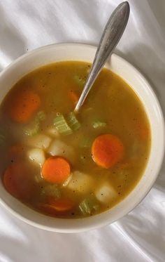 a bowl of soup with carrots, celery and potatoes on a white cloth