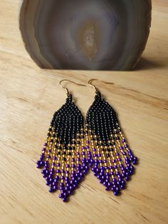 These beautiful fringe earrings are Indigenous handmade earrings made with glass toho seed beads, thread, and gold plated earring wires that are nickel free! They are a perfect pair of earrings to wear casually or on a night out! They are lightweight and would make a great gift for anyone special in your life, or as a gift to yourself! Each pair is wrapped with cardstock and washi tape, to ensure the earrings arrive in perfect condition to their destination:) Please message me for additional details or any questions you may have! Gold Dangle Earrings With Black Beads, Purple Beaded Dangle Earrings With Black Beads, Purple Dangle Beaded Earrings With Black Beads, Gold Beaded Fringe Earrings With Adjustable Fit, Purple And Gold Beaded Earrings, Artisan Purple Beaded Earrings, Black And Gold Fringe Earrings, Purple Fringe Earrings, Purple Dangle Earrings With Black Beads