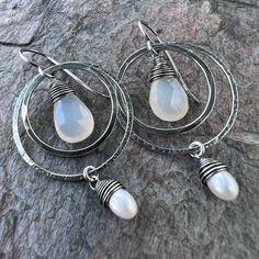 Two tiny genuine freshwater pearls are carefully wrapped in sterling silver wire. The white pearls dangle from sterling silver rings which I have formed, soldered, and hammered by hand. Inside the rings are natural Chalcedony teardrops. The earrings dangle from handformed Sterling Silver earwires. The silver has been oxidized and polished to create the patina finish. Be sure to see all photos and video for size and color reference. Total Earring Length: About 2 inches Silver Teardrop Earrings With Pearl Charm As Gift, Sterling Silver Teardrop Pearl Drop Jewelry, Silver Dangle Wire-wrapped Pearl Earrings, Nickel-free Teardrop Pearl Earrings In Sterling Silver, Sterling Silver Teardrop Dangle Earrings With Pearl Drop, Sterling Silver Teardrop Pearl Earrings With Charm, Handmade Drop Pearl Earrings In Sterling Silver, Handmade Sterling Silver Drop Pearl Earrings, Silver Wire Wrapped Pearl Earrings Gift