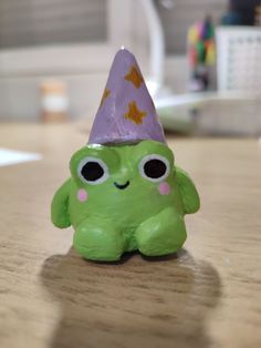 a green toy sitting on top of a wooden table with a purple hat on it's head