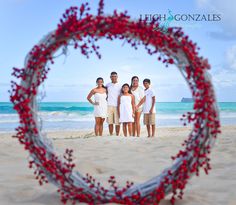 a group of people standing on top of a sandy beach next to the ocean in front of a heart shaped frame