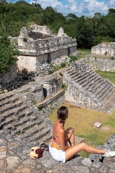 a woman sitting on top of a stone wall next to an ancient building with ruins