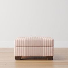 an upholstered footstool sitting on top of a hard wood floor next to a white wall