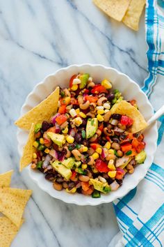 a white bowl filled with black eyed peas, corn and avocado salsa next to tortilla chips