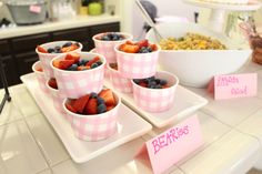 small cups filled with strawberries and blueberries on a table next to a bowl of cereal