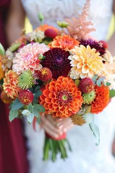 a bride holding a bouquet of flowers with orange and red colors in her hands on her wedding day