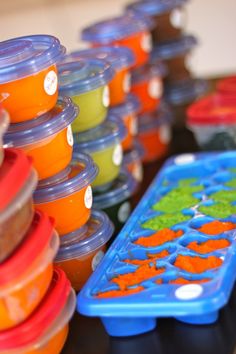 there are many plastic cups with different colors on the table and one is filled with oranges