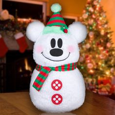 a white teddy bear with a green and red hat on it's head sitting in front of a christmas tree