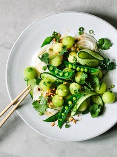 a white plate topped with cucumbers and green beans next to chopsticks