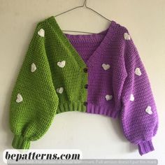 two knitted sweaters with hearts on them hanging from a hanger against a wall