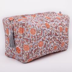 an orange and grey floral print bag with tassels on the front, sitting on a white surface