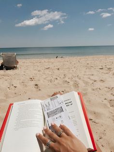 someone is reading a book on the beach with their hand resting on an open book