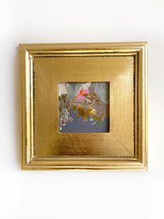 a gold framed photograph hanging on the wall with a pink bird in it's mouth