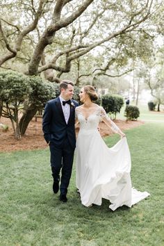 a bride and groom walking in the grass under some trees at their wedding reception venue