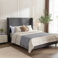 a bedroom with white walls and wood floors, a bed frame is made in grey fabric