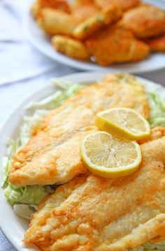 fish fillets on a white plate with lemon wedges