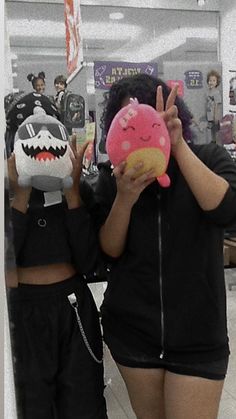 two people standing in a store holding up stuffed animals to their faces and making the peace sign