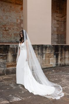 a woman in a wedding dress and veil standing on the street with an old brick building behind her