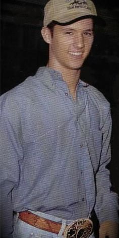 a young man wearing a baseball cap and blue shirt smiling at the camera with his hands in his pockets