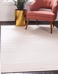 a white rug with a pink chair and potted plant in the corner next to it