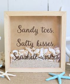 sand and seashells in a wooden frame on a table with starfish nearby