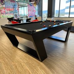 a black pool table in an office with graffiti on the walls and windows behind it