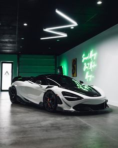 a white and black sports car parked in a garage next to a neon green wall