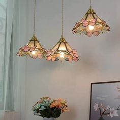 three light fixtures hanging from a ceiling in a room with white walls and flowers on the table