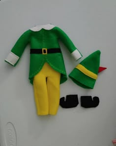 a green elf outfit with yellow pants and black shoes on top of a white surface